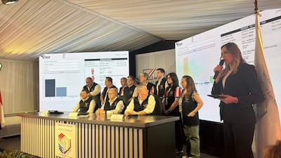 Luis Alberto Mauro con micrófono y traje oscuro, mientras Jorge Bogarín González lo observa. Ambiente formal con pantallas mostrando datos electorales.