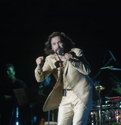 Marco Antonio Solís con traje claro, sosteniendo un micrófono y actuando intensamente en un escenario durante su concierto.
