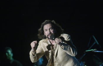 Marco Antonio Solís con traje claro, sosteniendo un micrófono y actuando intensamente en un escenario durante su concierto.