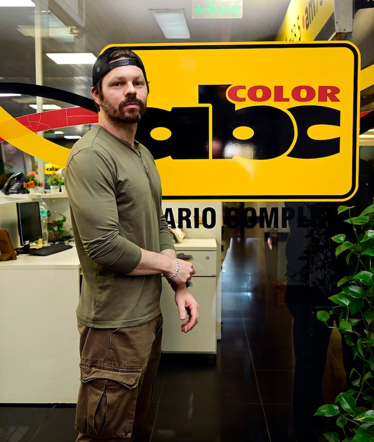 Blake Webb de pie, con barba y camiseta verde, frente al logo de ABC Color en un ambiente moderno y relajado.