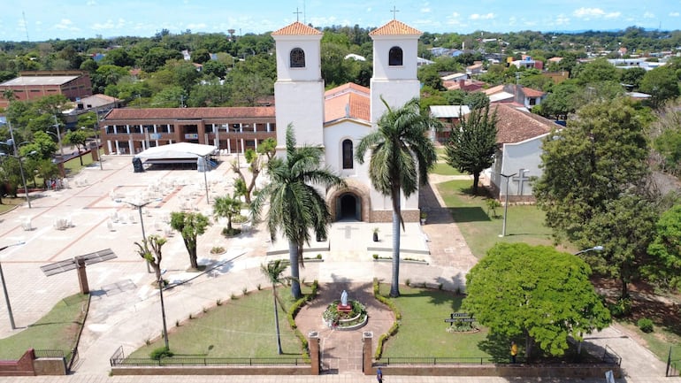 Iglesia de fachada blanca con torres y ambiente preparado para la celebración religiosa, con sillas y tarima cubierta.