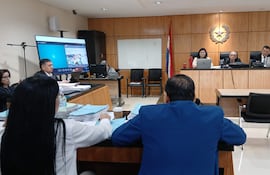 Mujer con gafas y hombre en saco azul en sala de juicio, escuchando atentamente mientras se revisan documentos.