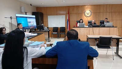 Mujer con gafas y hombre en saco azul en sala de juicio, escuchando atentamente mientras se revisan documentos.