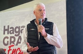 Arnoldo Wiens, con chaleco negro y camisa blanca, habla con micrófono ante un público, aparentemente reflexivo.