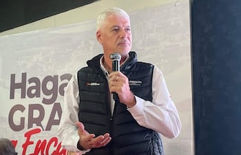 Arnoldo Wiens, con chaleco negro y camisa blanca, habla con micrófono ante un público, aparentemente reflexivo.