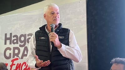 Arnoldo Wiens, con chaleco negro y camisa blanca, habla con micrófono ante un público, aparentemente reflexivo.