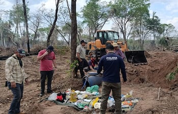 Grupo de policías antiescasteo y civiles revisan objetos en una zona rural desforestada, con retroexcavadora al fondo.