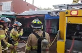Cuatro bomberos con cascos y trajes de intervención térmica en un ambiente urbano, junto a un camión amarillo.