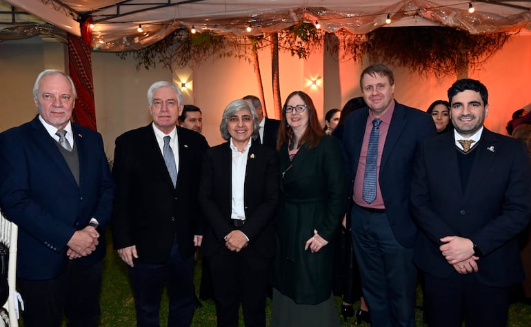 Grupo de seis personas en atuendo formal, sonriendo bajo una carpa decorada con luces cálidas.