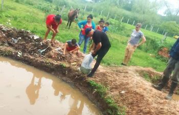 La productora Graciela Estigarribia acompañada de sus hijos y el Ing. Sergio Gómez, observa el momento del cultivo de los primeros alevines de tilapia en su estanque.