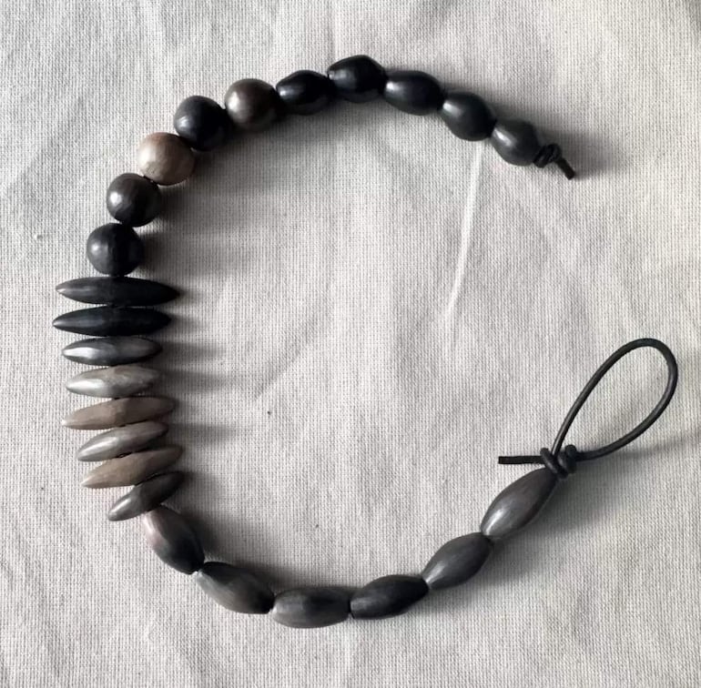 Collar elaborado con cuentas oscuras y simétricas, sobre una superficie clara, acentuando su diseño único.