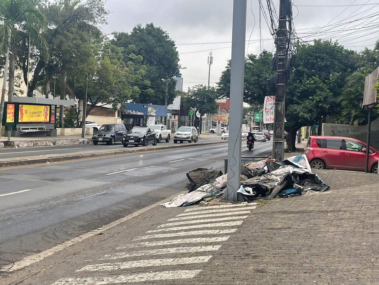 Escena urbana de Asunción con acumulación de basura y un panel publicitario, sin personas visibles, ambiente nublado.