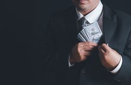 Un hombre guarda billetes de dólares en el bolsillo interno de su saco.