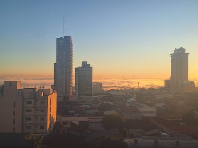 Paisaje urbano de Asunción con edificios altos y neblina al amanecer, creando una atmósfera tranquila.