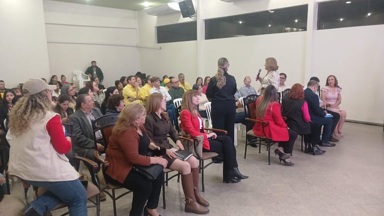 Cuatro mujeres en el panel del foro, una de pie con micrófono, mientras otros participantes toman notas en un ambiente formal.