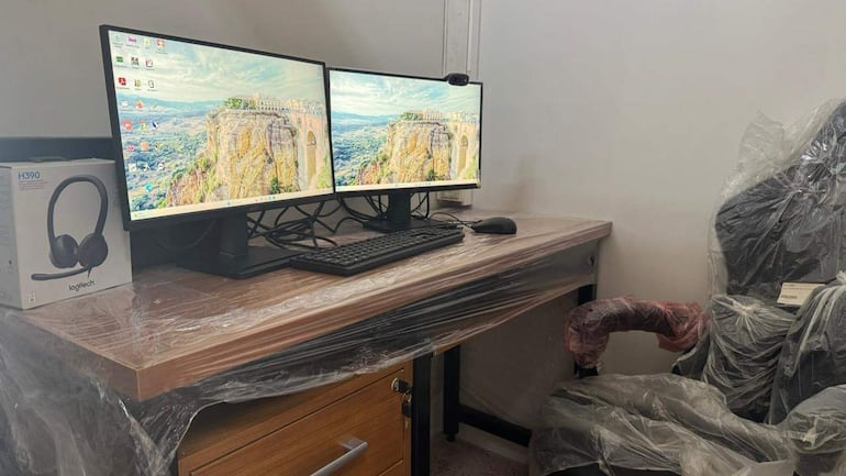 Espacio de oficina con escritorio, dos monitores encendidos mostrando paisajes, auricular Logitech H390 sobre la mesa.