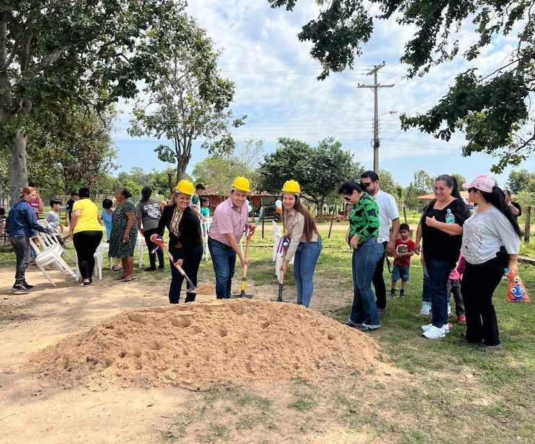 Richard Castiñeira y seis personas con cascos amarillos sonríen y sostienen palas en una ceremonia al aire libre, rodeados de espectadores.