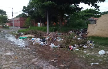 Una calle del barrio Silvio Pettirossi cubierta de basura y charcos de agua, con edificios de ladrillo al fondo.