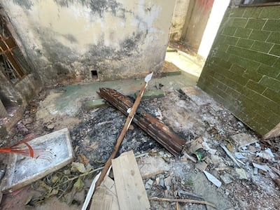 Espacio interior en abandono, con trozo de madera quemada y rastrillo junto a hojas secas y basura.