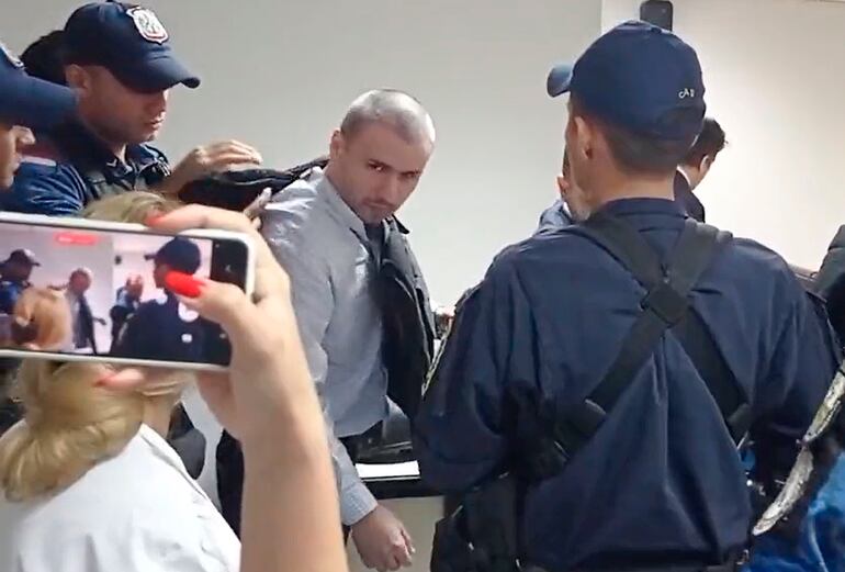 Un agente pone un chaleco antibalas al acusado Alberto Ayala Jacquet para su posterior retiro de la sala de juicio. 