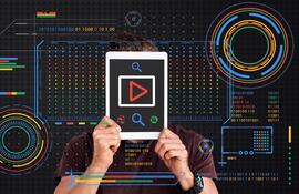 Hombre sosteniendo una tableta frente a su rostro con un botón de reproducción rojo en pantalla, rodeado de una interfaz digital futurista con gráficos HUD en los colores azul, rojo, amarillo y verde de Google.