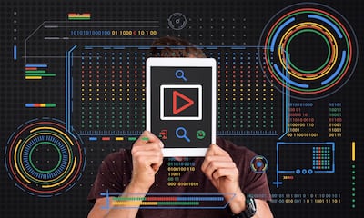 Hombre sosteniendo una tableta frente a su rostro con un botón de reproducción rojo en pantalla, rodeado de una interfaz digital futurista con gráficos HUD en los colores azul, rojo, amarillo y verde de Google.