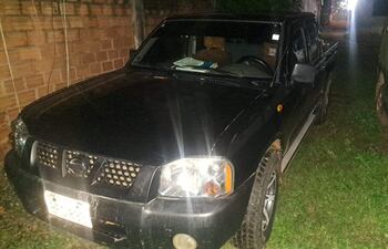 Camioneta Nissan Frontier negra estacionada fuera de un camino, rodeada de césped y otros vehículos, sin personas visibles.