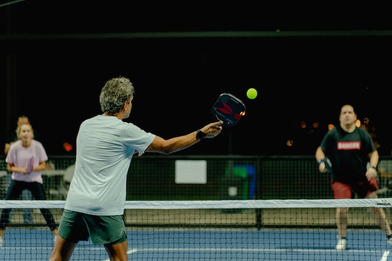 El pickleball se practica en una cancha más pequeña que la de tenis, con paletas sólidas y una pelota plástica perforada.