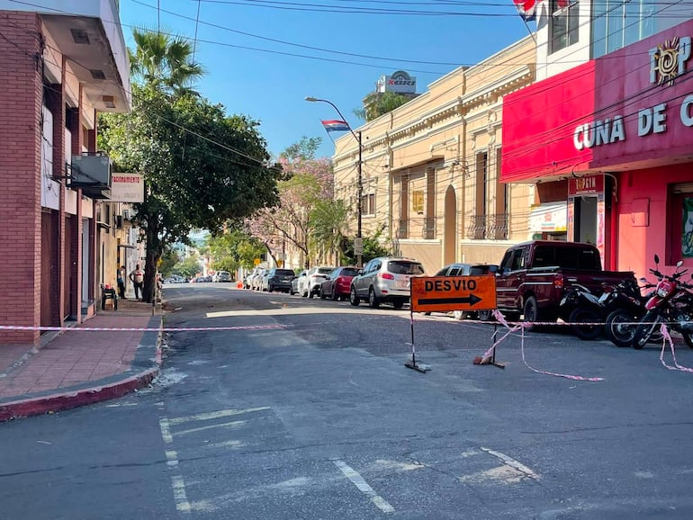 Calle con tráfico restringido y un cartel de desvío. Edificio rojo visible al fondo, ambiente urbano y despejado.