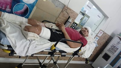 Hombre en camilla con venda en la cabeza y lesiones visibles, usando un teléfono móvil en un ambiente médico.