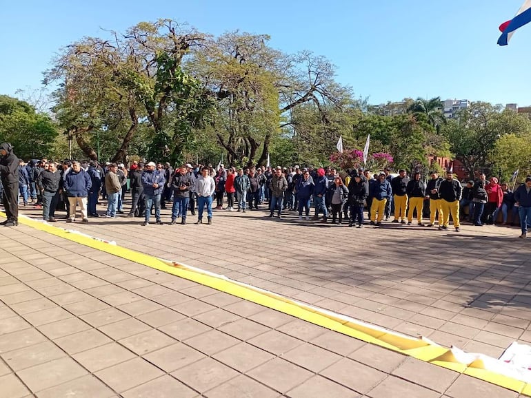 Grupo de personas con abrigos oscuros, algunos con brazos cruzados, otros con manos en bolsillos, en un entorno de parque durante protestas.