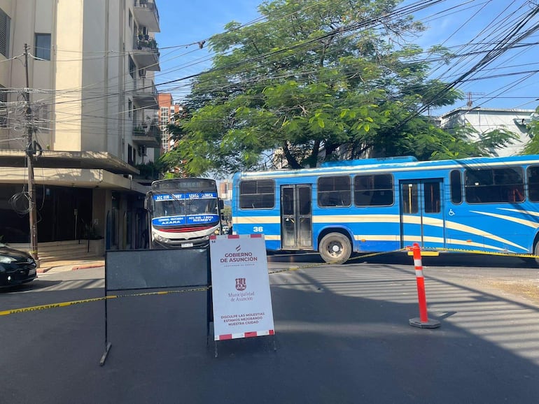 Cartel de Gobierno de Asunción y vallas en intersección sin personas visibles, con dos autobuses de transporte público.