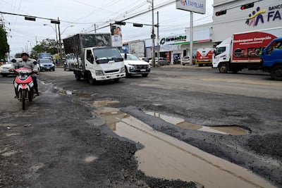 Motociclista cauteloso en la intersección, camión de carga cruzando, cielo nublado y charcos en el pavimento agrietado.