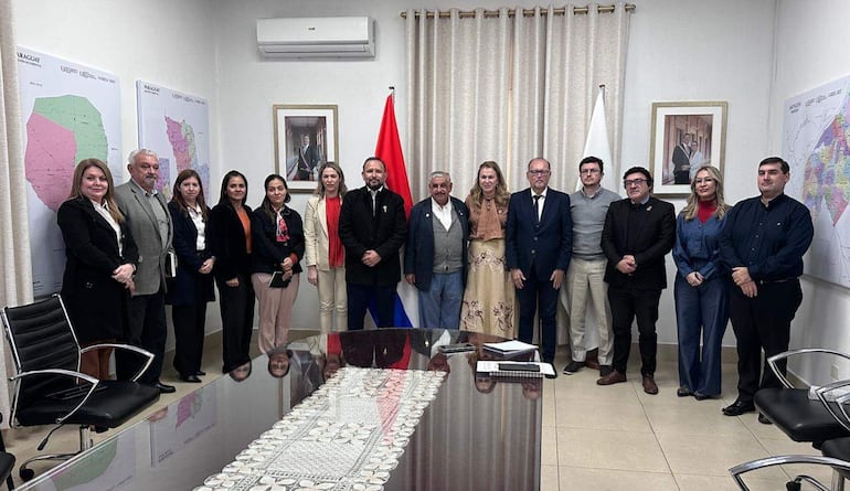Isaías Ricardo Fretes y María Teresa Barán en reunión, rodeados de personas en un ambiente formal con mapas y banderas de Paraguay.