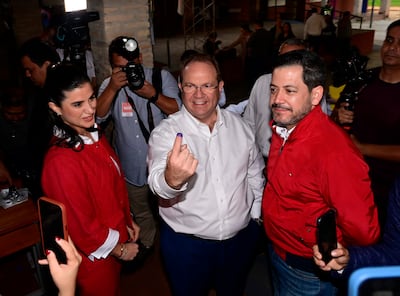 Constanza Troche sonríe vestida de rojo, mientras Camilo Pérez López Moreira muestra su dedo con tinte violeta en camiseta blanca.