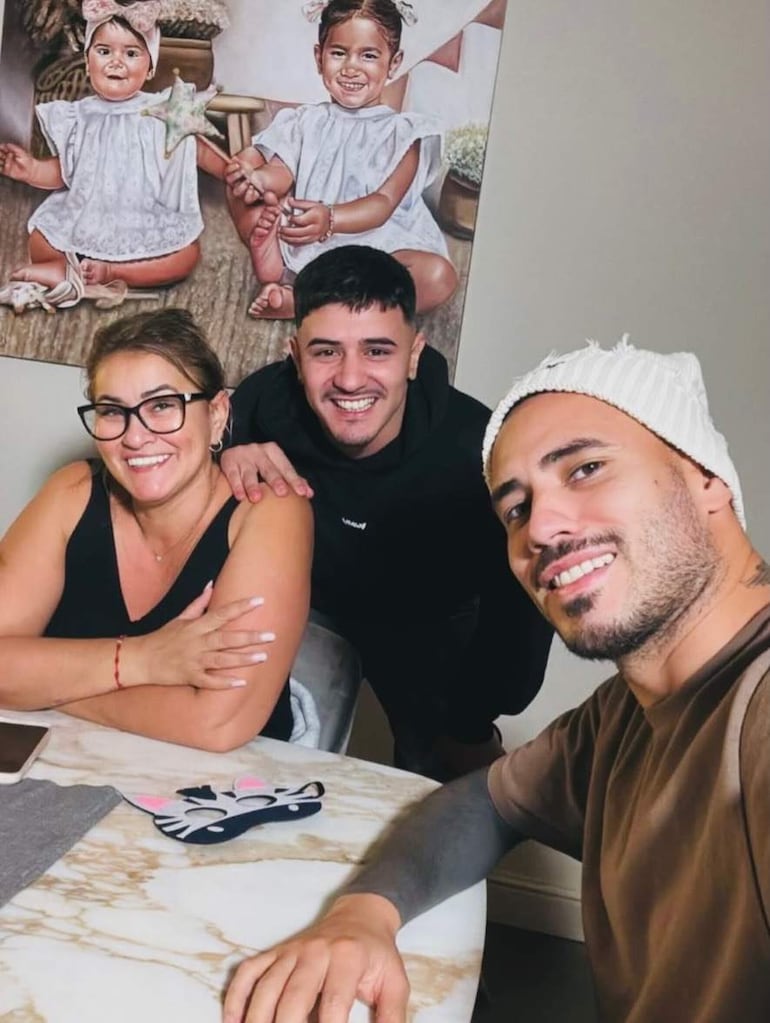 Antonio Sanabria, con gorro blanco y cabello corto, sonríe junto a una mujer con gafas y un hombre con atuendo oscuro.