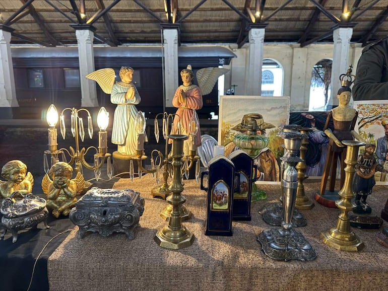 Mesa con figuras de ángeles, candelabros dorados y pinturas clásicas en un interior antiguo.