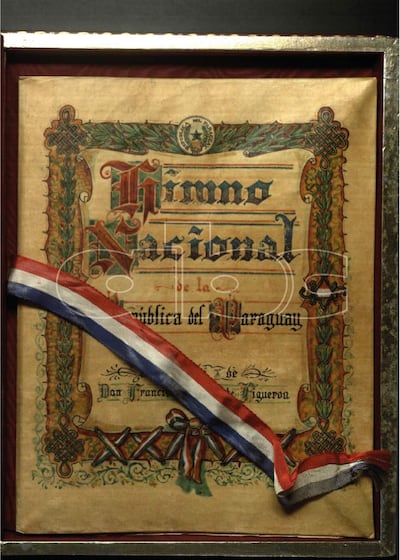 Documento enmarcado titulado 'Himno Nacional de la República del Paraguay' con diseño decorativo y cinta tricolor.