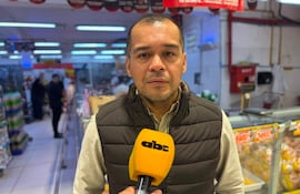 Hombre de chaqueta oscura y camisa clara sostiene micrófono amarillo de ABC Color, entrevistado en un supermercado lleno de productos.