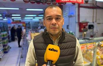 Hombre de chaqueta oscura y camisa clara sostiene micrófono amarillo de ABC Color, entrevistado en un supermercado lleno de productos.