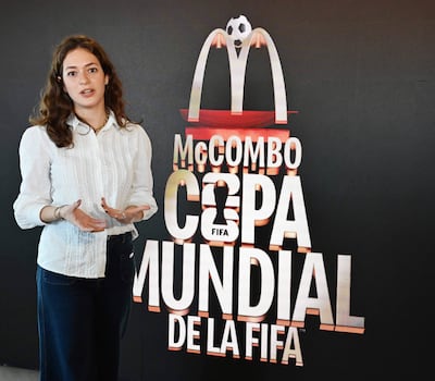 Mujer de cabello rizado y castaño, con camisa blanca y pantalones oscuros, presenta el McCombo Copa Mundial de la FIFA.