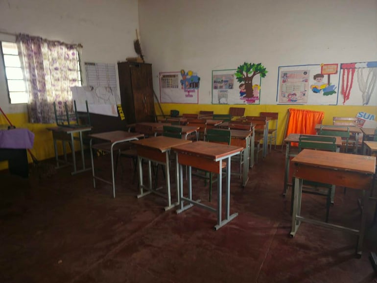Aula vacía con escritorios y sillas desordenadas, carteles decorativos en paredes coloridas, ausencia de estudiantes.