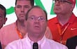 Camilo Pérez con gafas y camisa blanca sostiene un micrófono mientras habla, rodeado de tres hombres en un evento formal.