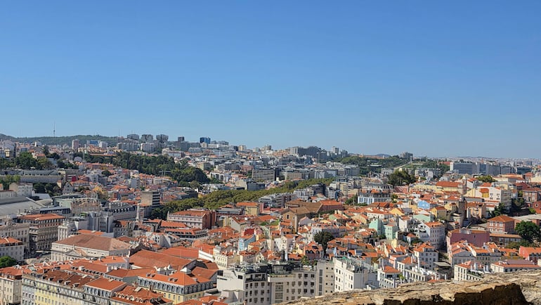 Ciudad de Lisboa con edificios de diversos estilos y techos anaranjados bajo un cielo despejado.