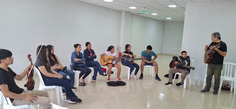 Grupo en taller de música con guitarras y un violín, presentan expresiones tranquilas mientras un adulto instruye.