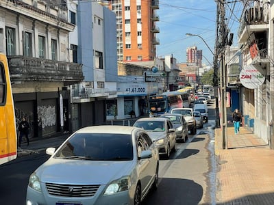 Calle urbana concurrida, dos transeúntes casuales, edificios varios y letrero de la pizzería Zampanò visible.