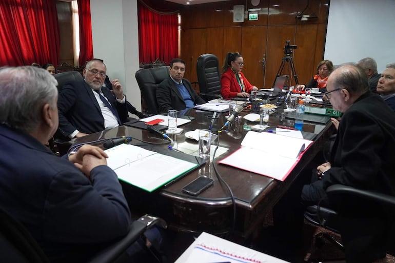José Emilio Argaña Contreras habla ante otros asistentes en sala con paredes de madera y mesa con documentos.