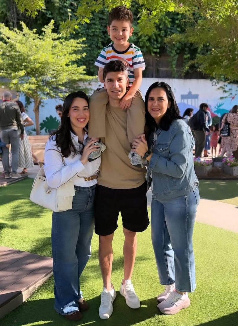 Francisco Gómez sonríe mientras sostiene a un niño con camiseta de rayas, acompañado de mujeres sonriendo en un entorno verde.