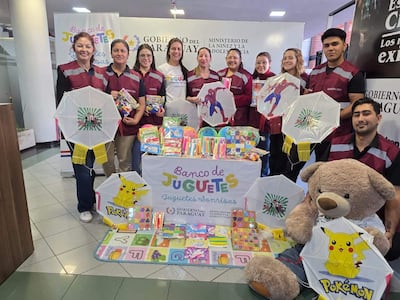 Grupo de ocho personas con camisetas maroon y gris sosteniendo juguetes y cometas en ambiente amigable.