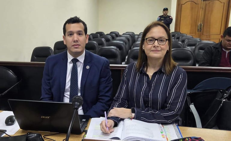 Benítez, con traje oscuro, y Sánchez, con camisa de rayas, sentados frente a un micrófono en un tribunal, tomando notas.